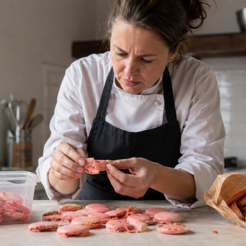 Chef examinant des coques de macarons roses dans une cuisine professionnelle